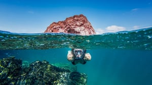 A traveler snorkeling underwater with a volcanic islet visible above the waterline in the Galápagos.