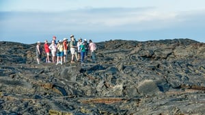 A small group of travelers standing on a wide volcanic lava field during a guided excursion in the Galapagos.