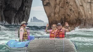 Two travelers wearing life jackets on a Zodiac boat with a guide, navigating between dramatic rock formations in the Galapagos.