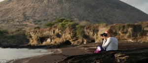 Egas Port in Santiago Island wit rocky beach and tourist taking pictures, background of volcano