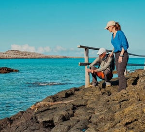Galapagos Legend Itinerary East Expedition: A couple taking a picture to a marine iguana