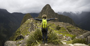 Traveler with a green backpack standing with open arms, overlooking Machu Picchu’s ancient Inca ruins in Peru.